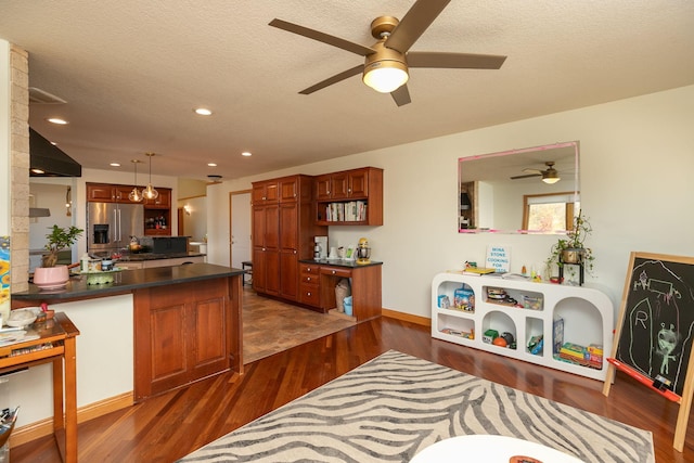 interior space with a ceiling fan, high quality fridge, dark wood finished floors, a peninsula, and dark countertops