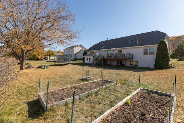view of yard featuring a deck, a trampoline, a garden, and stairs