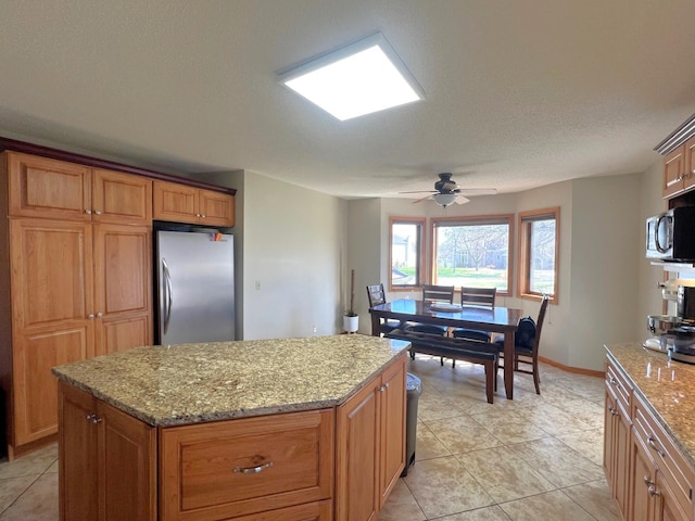 kitchen with stainless steel appliances, a kitchen island, light tile patterned floors, a ceiling fan, and a textured ceiling