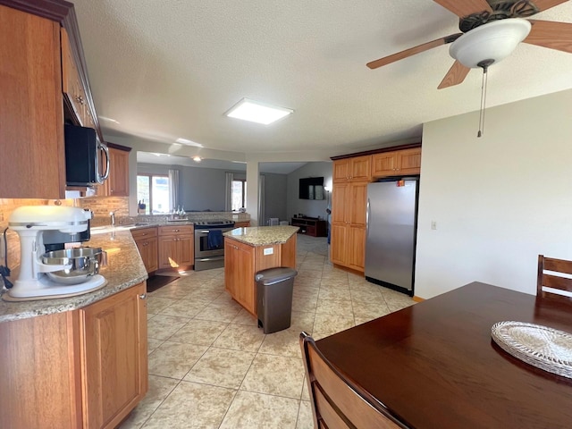 kitchen with appliances with stainless steel finishes, a sink, a kitchen island, light tile patterned flooring, and a peninsula