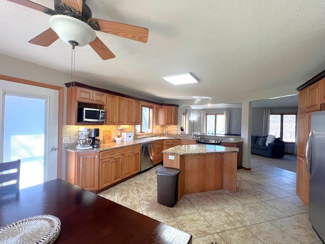 kitchen with appliances with stainless steel finishes, a center island, a textured ceiling, decorative backsplash, and healthy amount of natural light