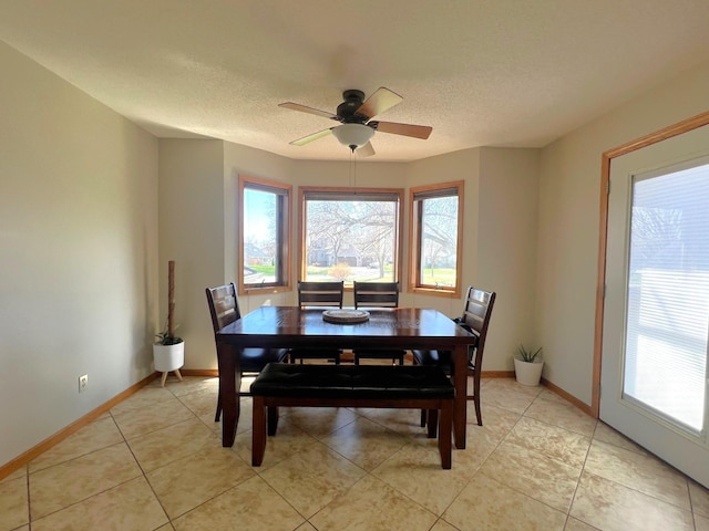 dining space featuring plenty of natural light, a ceiling fan, baseboards, a textured ceiling, and light tile patterned flooring