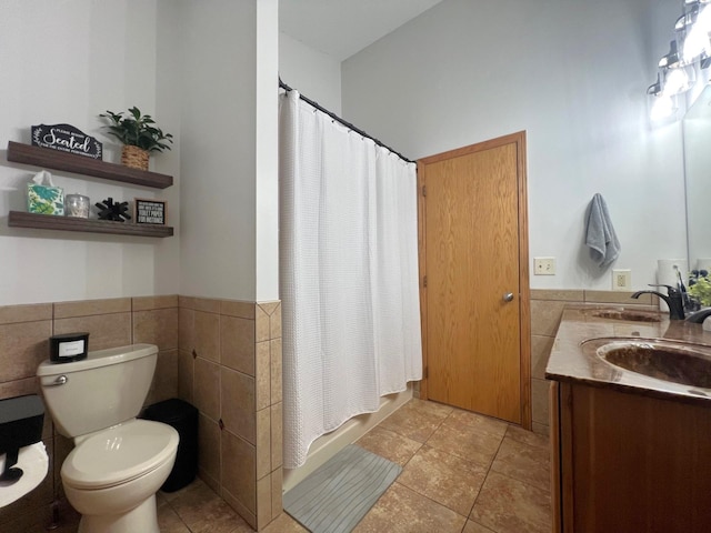 full bathroom featuring tile walls, toilet, tile patterned flooring, a wainscoted wall, and double vanity