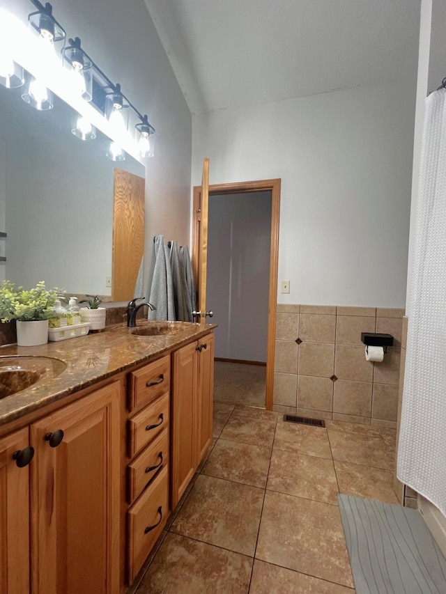 bathroom with tile patterned floors, double vanity, wainscoting, and tile walls