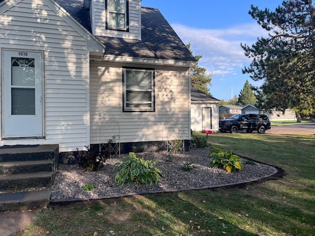 view of side of property featuring a lawn, roof with shingles, and entry steps