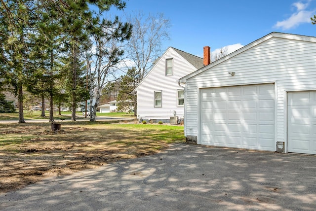 view of side of property with aphalt driveway, a chimney, and cooling unit