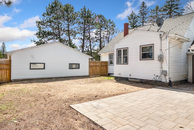 back of property with fence, a patio, a chimney, and a shingled roof