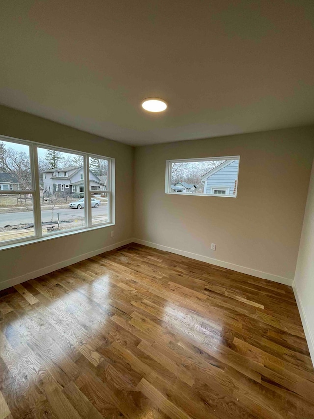 empty room featuring plenty of natural light, recessed lighting, baseboards, and wood finished floors