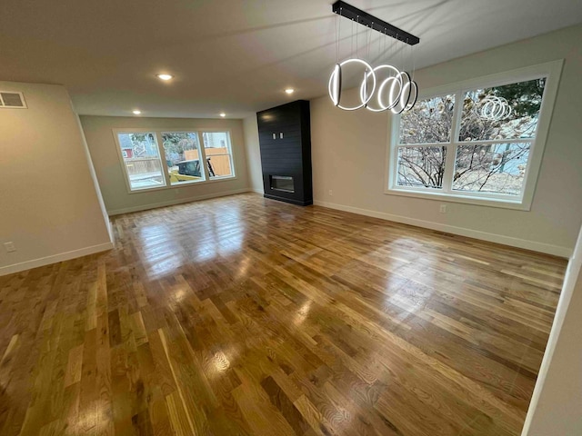 unfurnished living room with baseboards, a notable chandelier, wood finished floors, and visible vents
