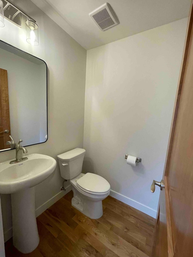 bathroom with baseboards, toilet, wood finished floors, and visible vents