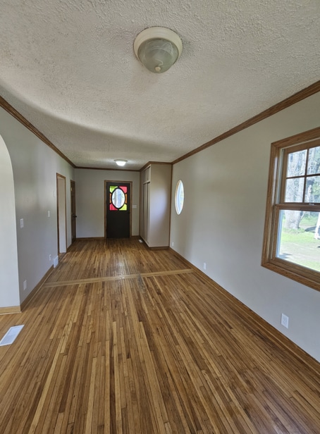 unfurnished living room featuring visible vents, ornamental molding, arched walkways, and hardwood / wood-style floors