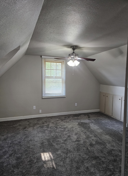 bonus room featuring a ceiling fan, vaulted ceiling, dark colored carpet, and a textured ceiling