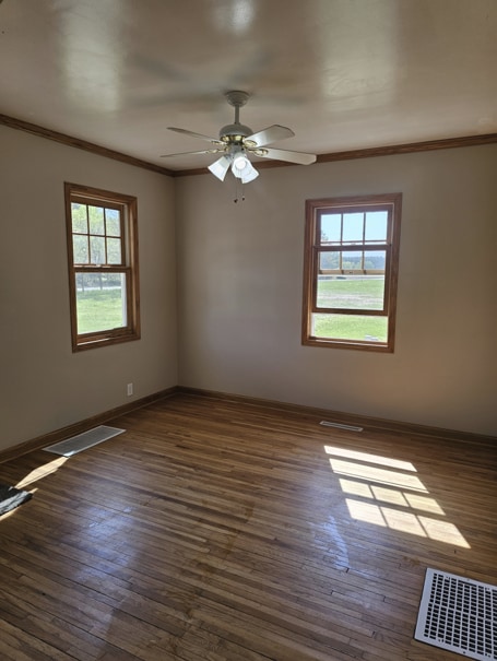 spare room featuring crown molding, baseboards, dark wood-type flooring, and visible vents