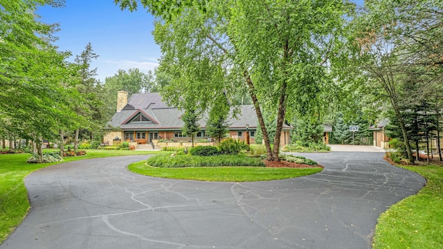 view of front of house with curved driveway, a front lawn, and a chimney