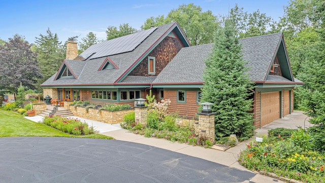 view of front of house featuring driveway, solar panels, roof with shingles, and a chimney