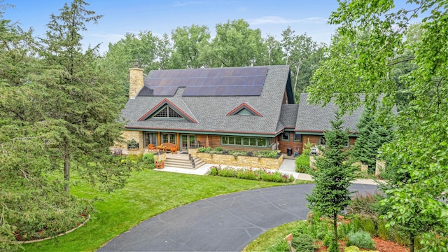 view of front of home featuring a porch, a chimney, a front yard, roof mounted solar panels, and a shingled roof