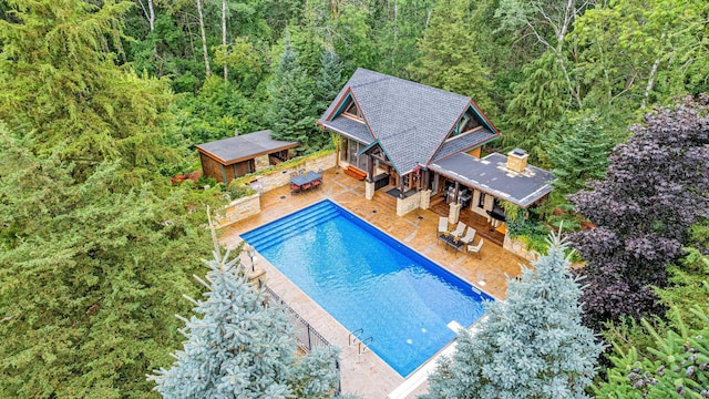 outdoor pool featuring a view of trees, an outbuilding, and a patio area