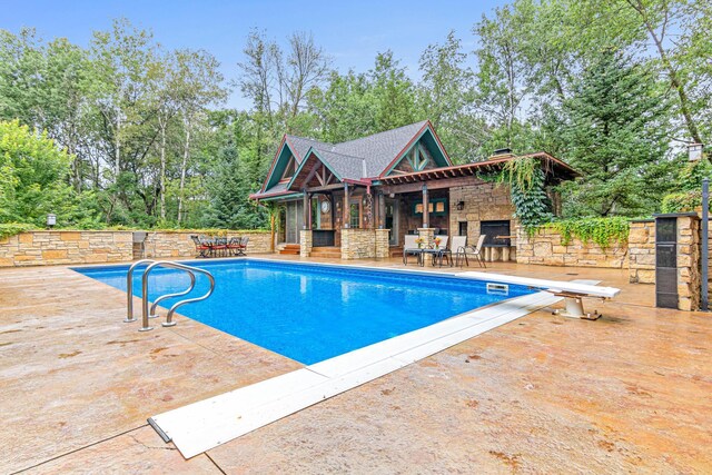 view of pool featuring an outdoor stone fireplace, a diving board, a patio area, and a fenced in pool