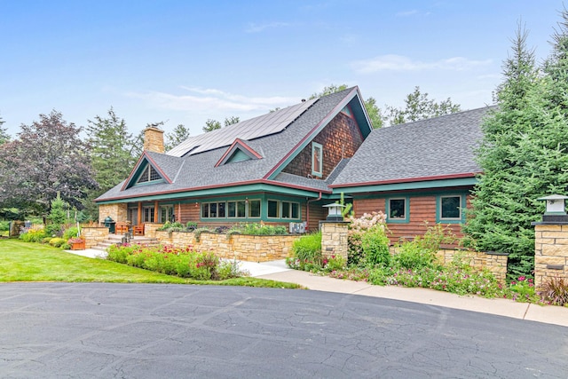 view of front of house featuring a porch, a shingled roof, a chimney, and roof mounted solar panels