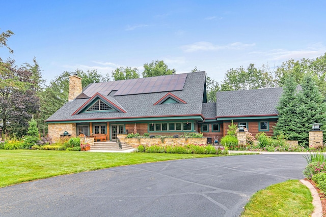 view of front facade featuring french doors, solar panels, a front yard, a chimney, and a shingled roof