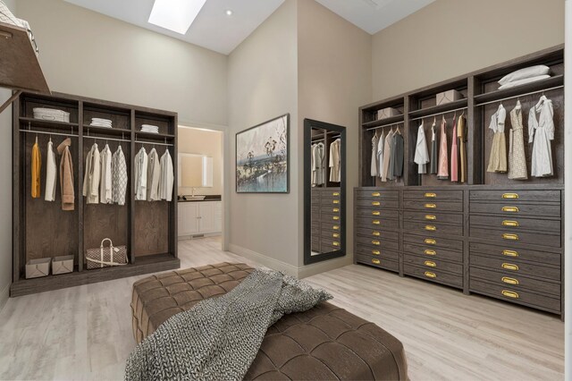 bedroom featuring a skylight, light wood-style flooring, a towering ceiling, baseboards, and ensuite bathroom