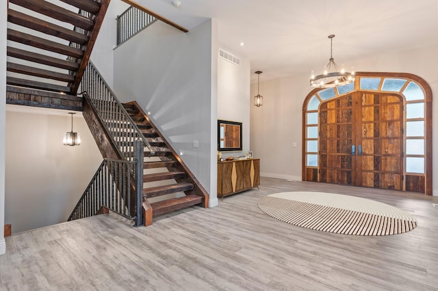 entrance foyer with a chandelier, wood finished floors, a towering ceiling, baseboards, and stairs