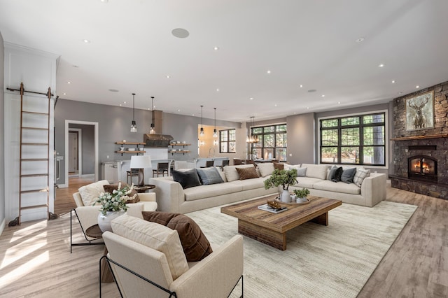 living room with a barn door, light wood-type flooring, recessed lighting, and a stone fireplace
