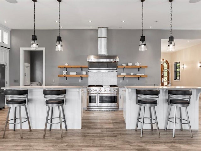 kitchen featuring range with two ovens, a center island with sink, open shelves, light wood-style floors, and recessed lighting