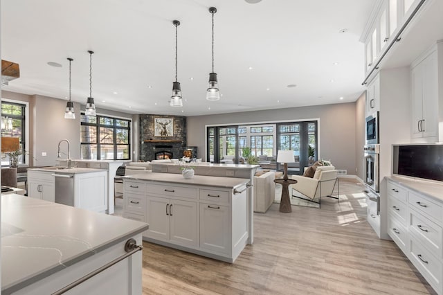 kitchen with open floor plan, an island with sink, appliances with stainless steel finishes, a stone fireplace, and recessed lighting