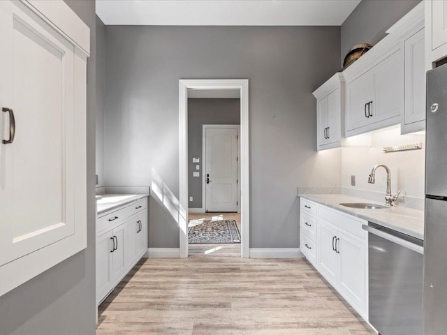 kitchen featuring stainless steel appliances, a sink, light wood finished floors, and white cabinetry