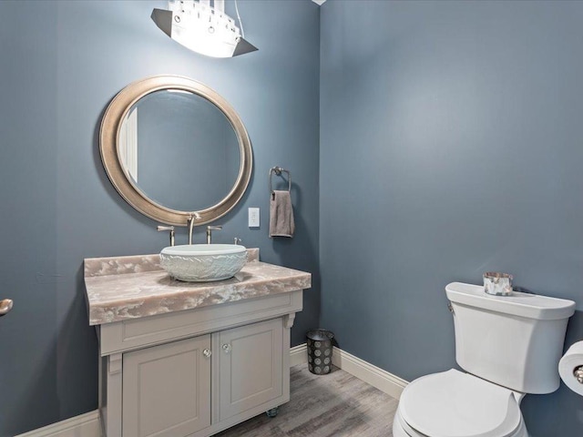 half bath featuring toilet, baseboards, wood finished floors, and vanity