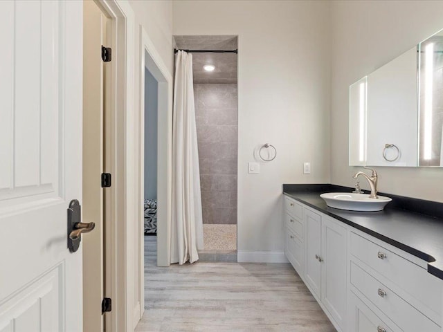 bathroom featuring a tile shower, vanity, wood finished floors, and baseboards