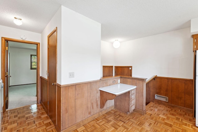 kitchen featuring a wainscoted wall, a textured ceiling, wooden walls, a peninsula, and light countertops