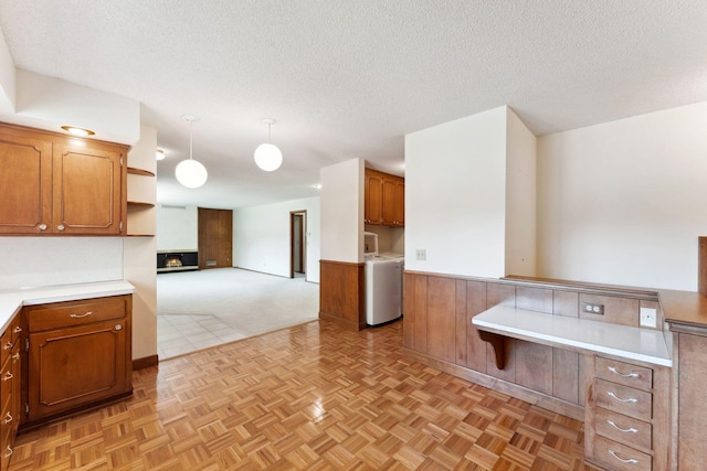 kitchen with washer / dryer, brown cabinets, light countertops, open floor plan, and a textured ceiling