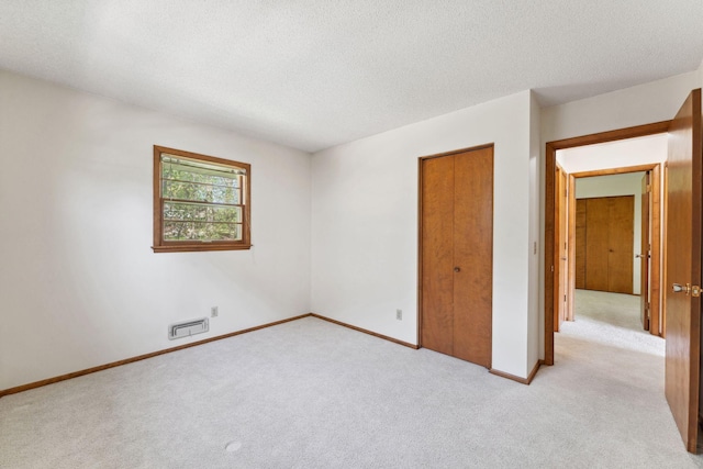 unfurnished bedroom featuring light carpet, a textured ceiling, baseboards, and a closet