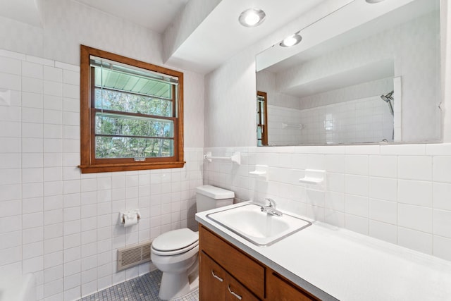 bathroom featuring toilet, a shower, tile walls, vanity, and tile patterned floors