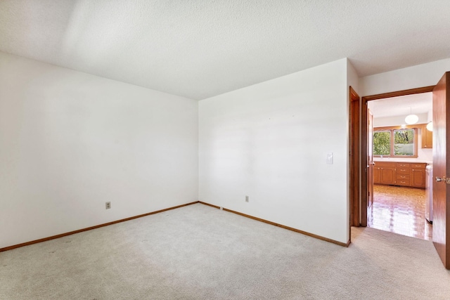 spare room with light colored carpet, baseboards, a textured ceiling, and a sink