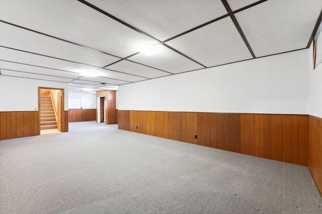 finished basement featuring a wainscoted wall, wood walls, stairs, and carpet flooring