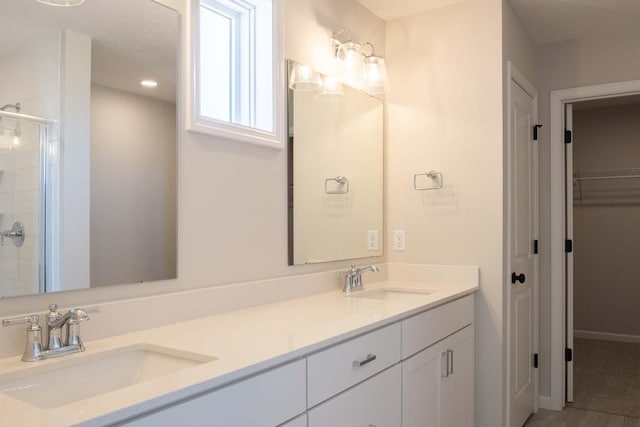 full bath with double vanity, a sink, a walk in closet, and a stall shower