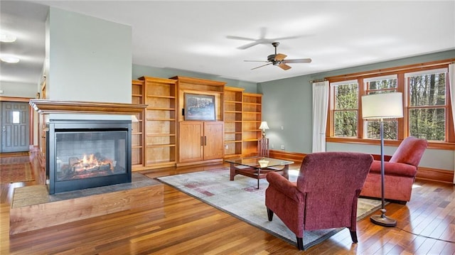 living area featuring wood-type flooring, baseboards, ceiling fan, and a glass covered fireplace