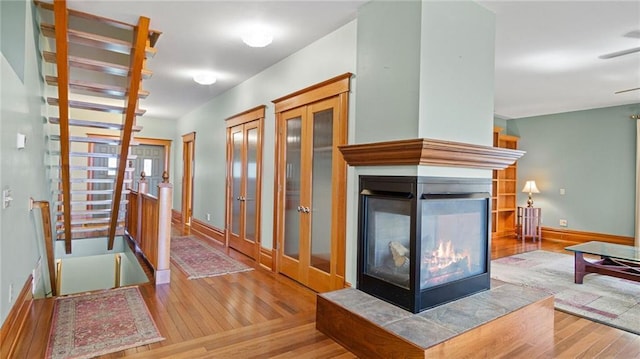 unfurnished living room featuring baseboards, a multi sided fireplace, wood finished floors, and french doors
