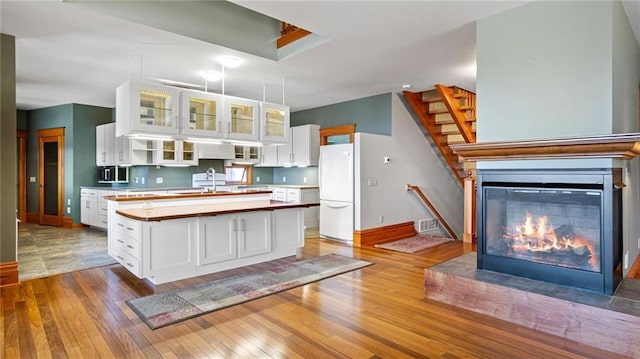 kitchen with freestanding refrigerator, hardwood / wood-style floors, glass insert cabinets, baseboards, and white cabinetry