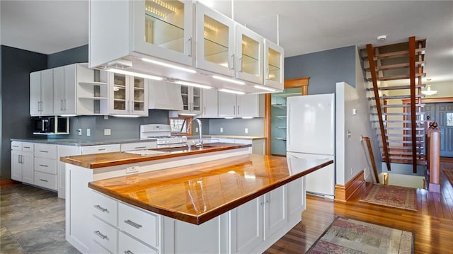 kitchen featuring white appliances, white cabinetry, wood counters, and a center island with sink