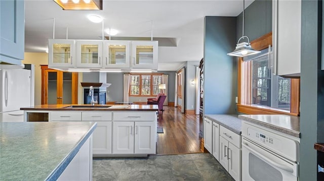 kitchen featuring white appliances, glass insert cabinets, white cabinets, a sink, and hanging light fixtures