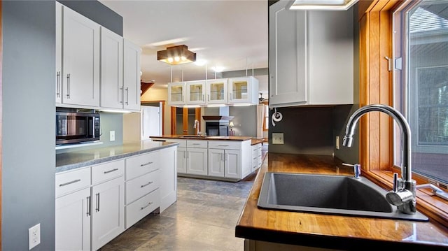 kitchen featuring a sink, butcher block counters, white cabinets, and glass insert cabinets
