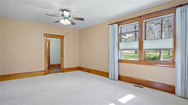 empty room featuring carpet floors, baseboards, a ceiling fan, and visible vents