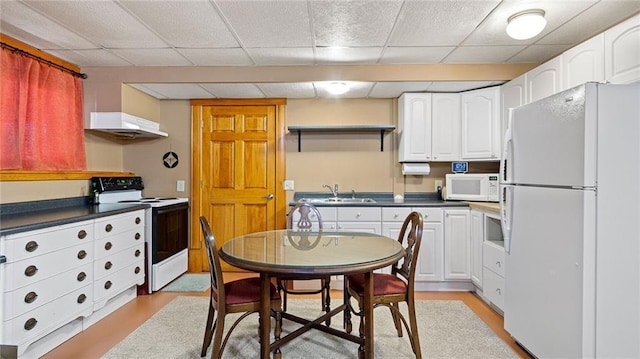 kitchen featuring white appliances, dark countertops, under cabinet range hood, and white cabinets
