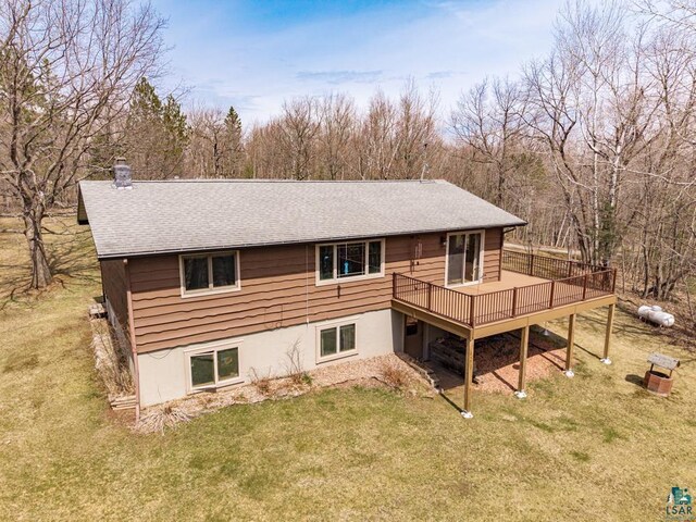 rear view of property with a lawn, roof with shingles, a wooden deck, and a chimney