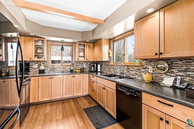 kitchen with dark countertops, a sink, light brown cabinets, dishwasher, and wood finished floors