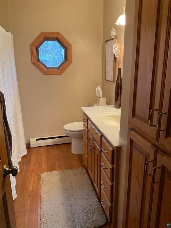 bathroom with wood finished floors, curtained shower, vanity, a baseboard radiator, and toilet